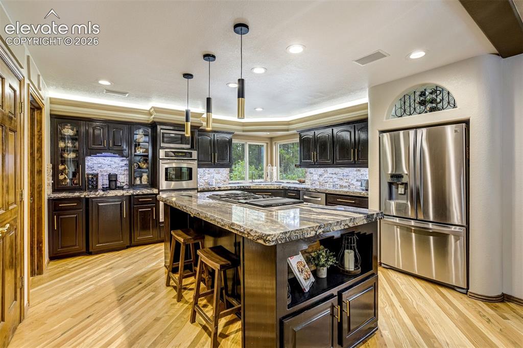 Image 12 of 40: Kitchen featuring wood-finish flooring, dark wood cabinetry, stainless stee