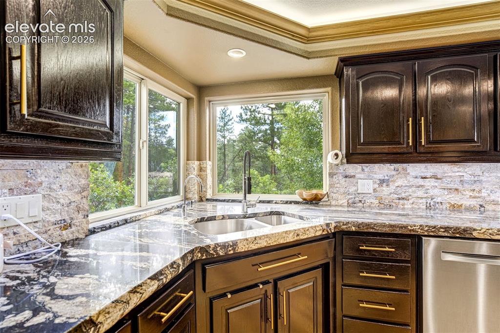 Image 14 of 40: Dark wood cabinetry with gold-tone hardware, granite countertops, tile back