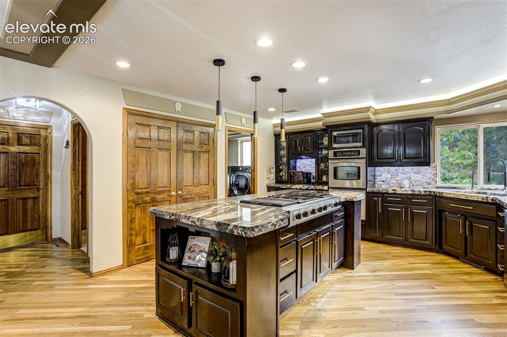 Image 15 of 40: Kitchen featuring a large island with a cooktop, dark wood cabinetry, integ