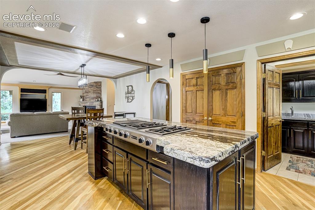 Image 16 of 40: Kitchen island with a built-in gas cooktop, granite countertop, recessed li