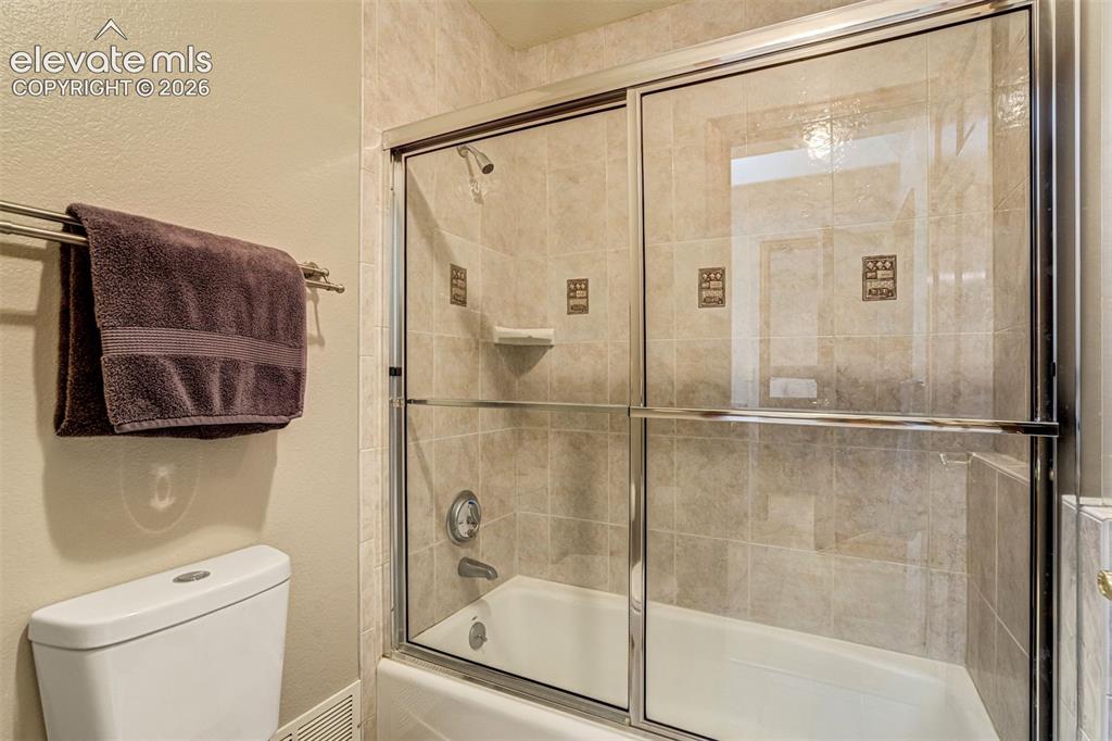 Image 28 of 40: Tub and shower combination with glass sliding doors, tiled surround, and in
