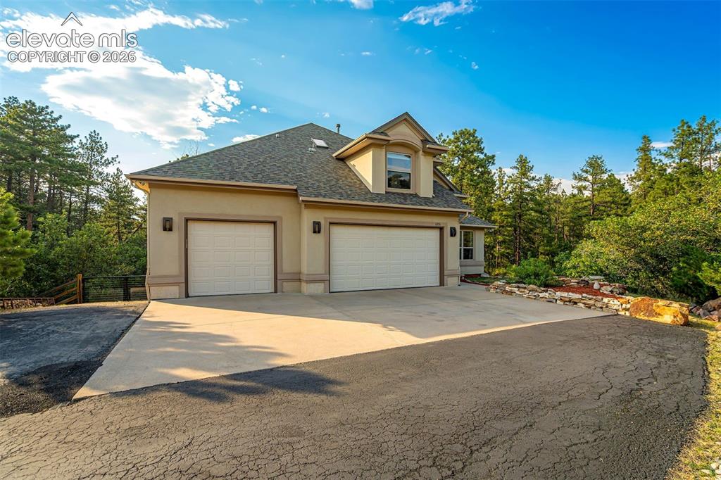 Image 3 of 40: Stucco exterior with a dormer window, two garage bays, concrete driveway, a
