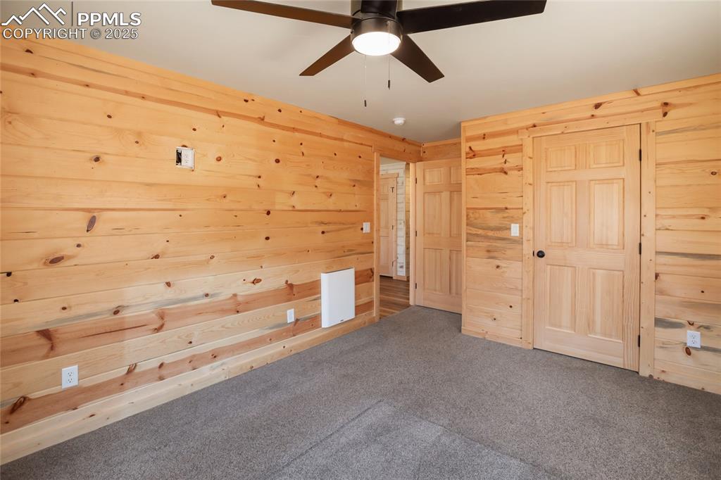 Image 18 of 45: Unfurnished bedroom featuring wood walls, carpet flooring, and ceiling fan
