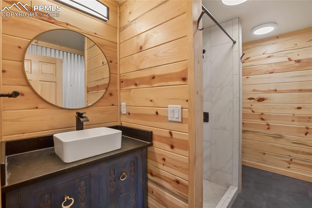Image 19 of 45: Main level full bathroom with wood walls, vanity, and a walk in shower
