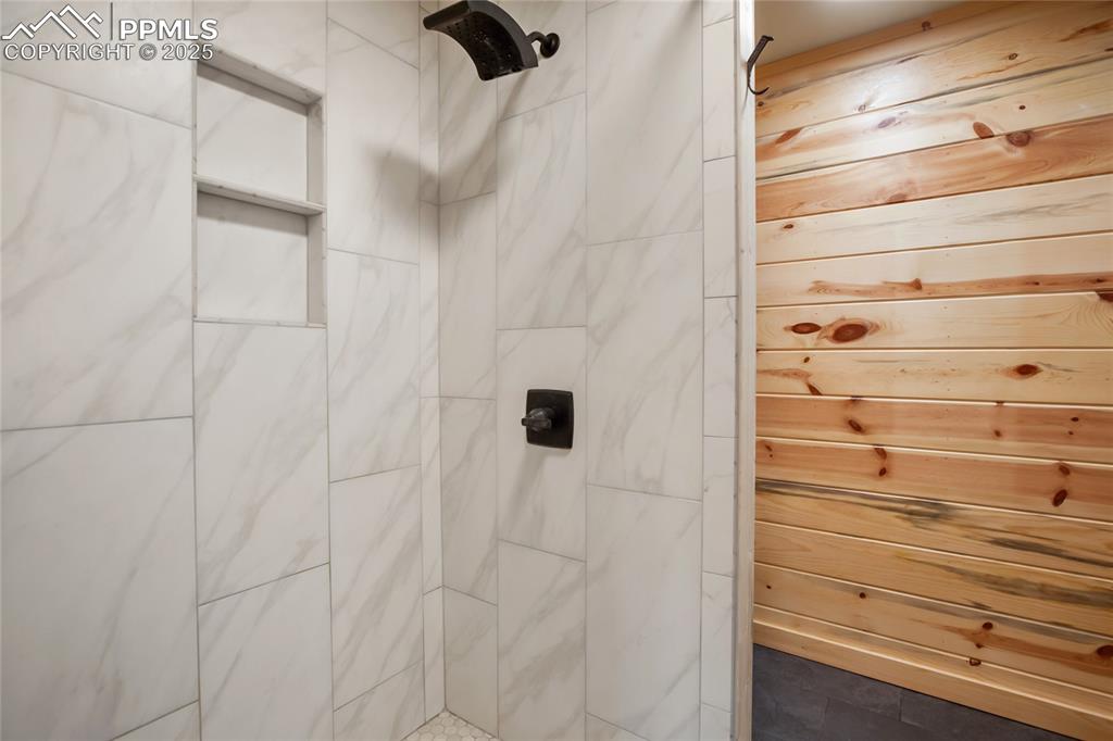 Image 20 of 45: Bathroom featuring a tile shower and wood walls