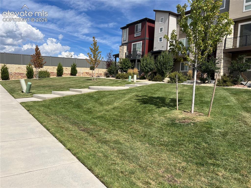 Image 3 of 35: Manicured lawn with young trees, concrete sidewalks, and multi-story reside