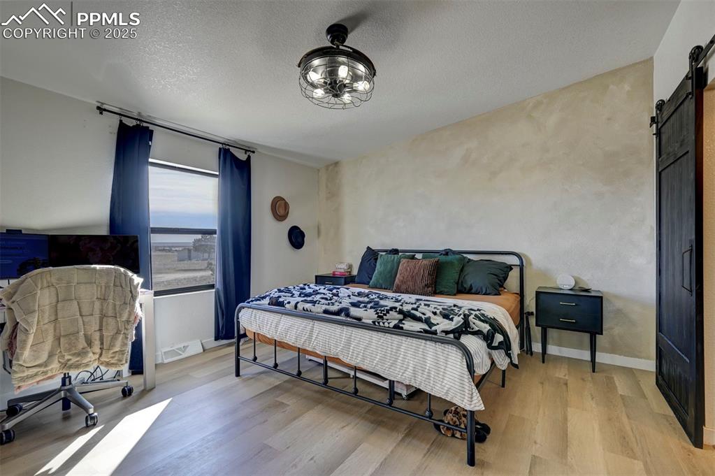 Image 15 of 40: Bedroom featuring a barn door, light wood-type flooring, and a textured cei