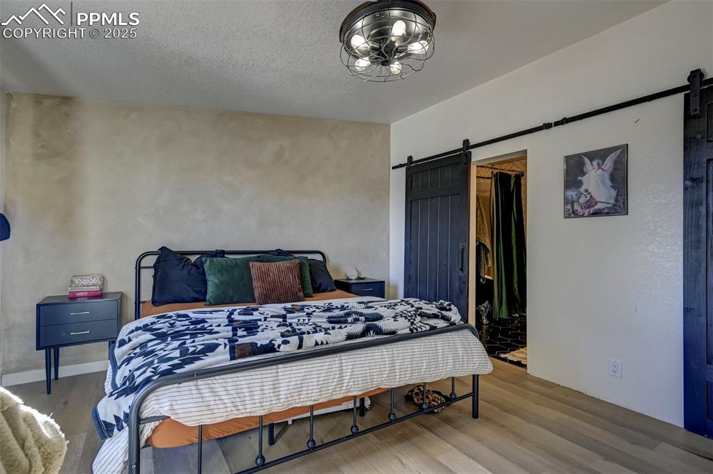 Image 16 of 40: Bedroom with a barn door, wood finished floors, and a textured ceiling