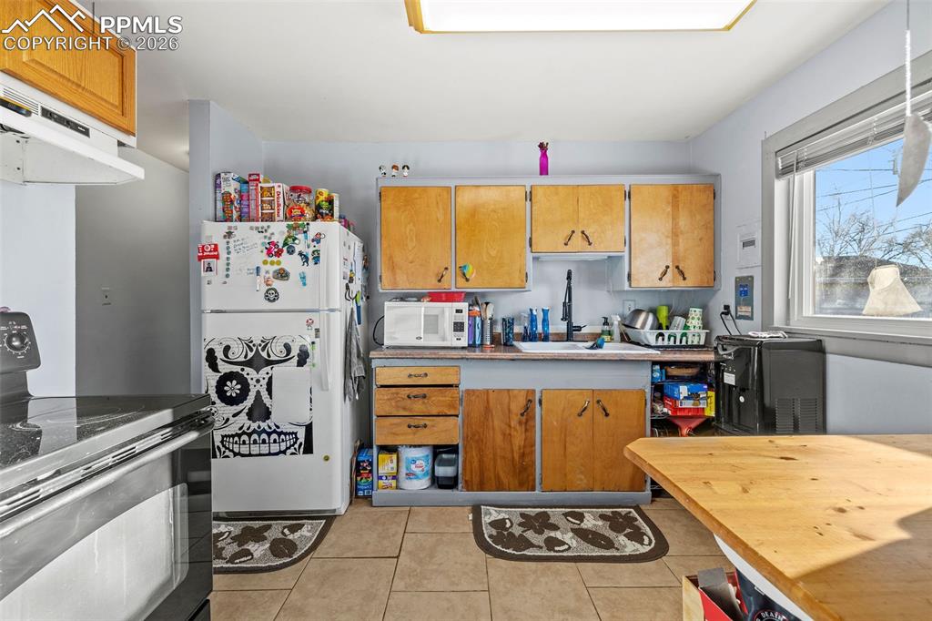 Image 10 of 19: Kitchen with white appliances, light tile patterned flooring, brown cabinet