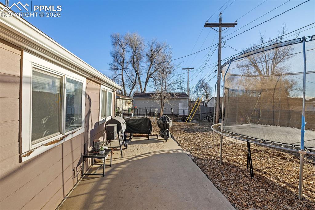 Image 17 of 19: Fenced backyard with a trampoline and a patio