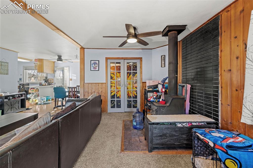 Image 8 of 19: Living room featuring wooden walls, french doors, a wood stove, wainscoting