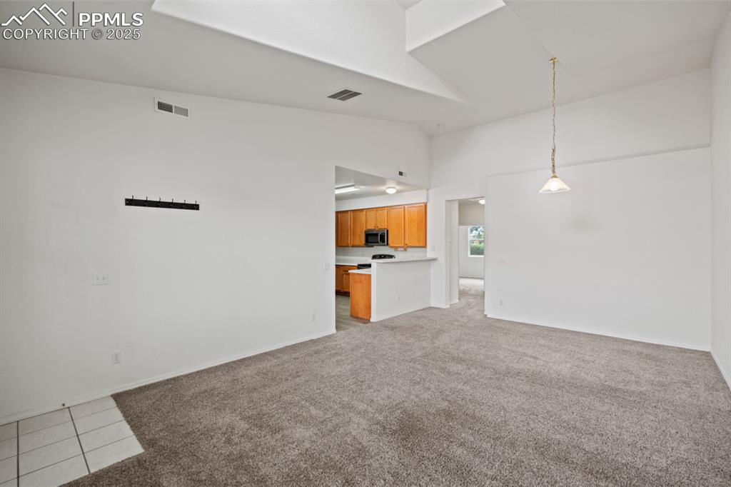 Image 10 of 22: Unfurnished living room with high vaulted ceiling and light colored carpet