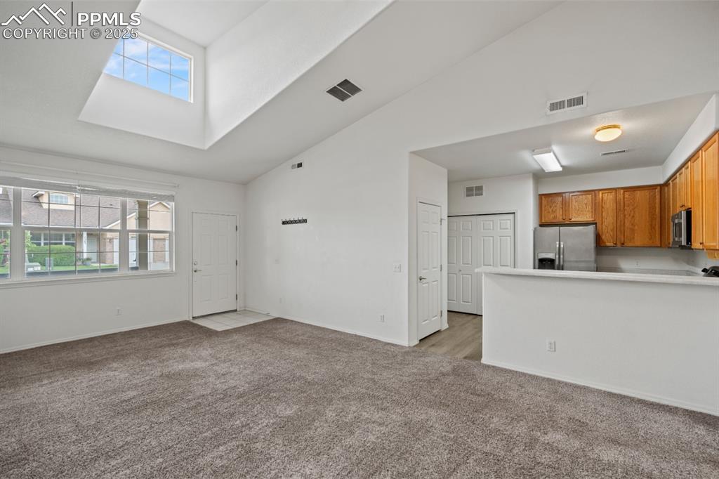 Image 6 of 22: Unfurnished living room with light carpet, high vaulted ceiling, a skylight