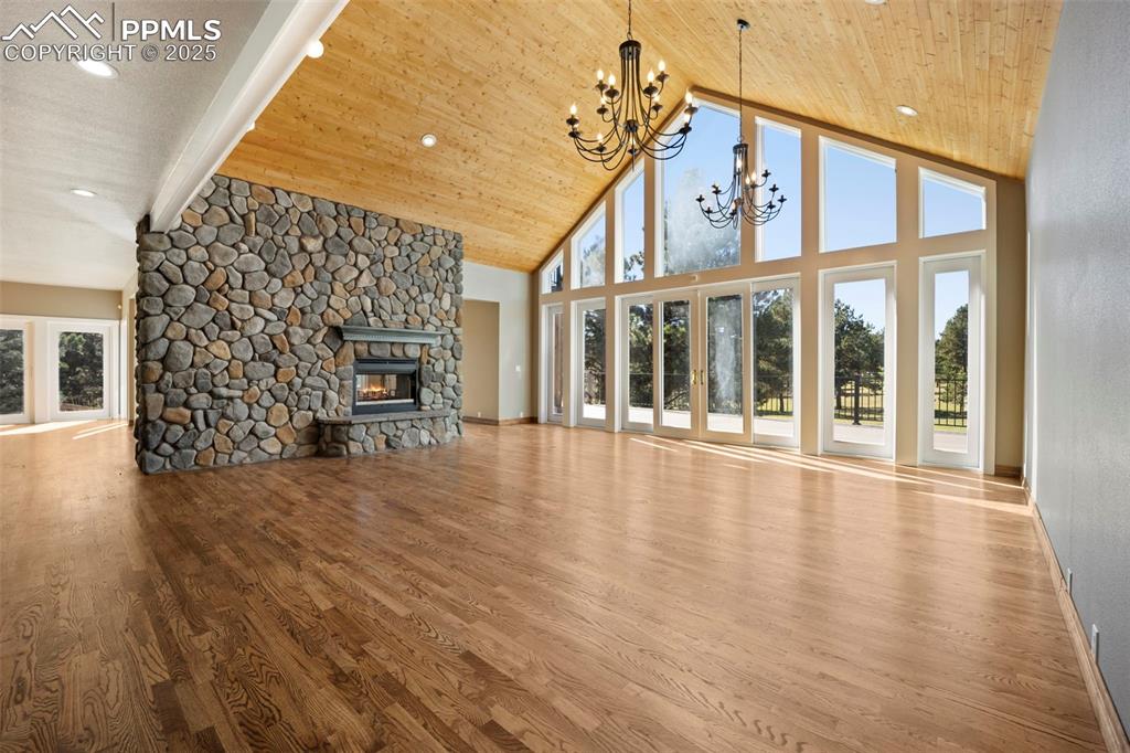 Image 17 of 50: Unfurnished living room featuring a stone fireplace, a chandelier, high vau