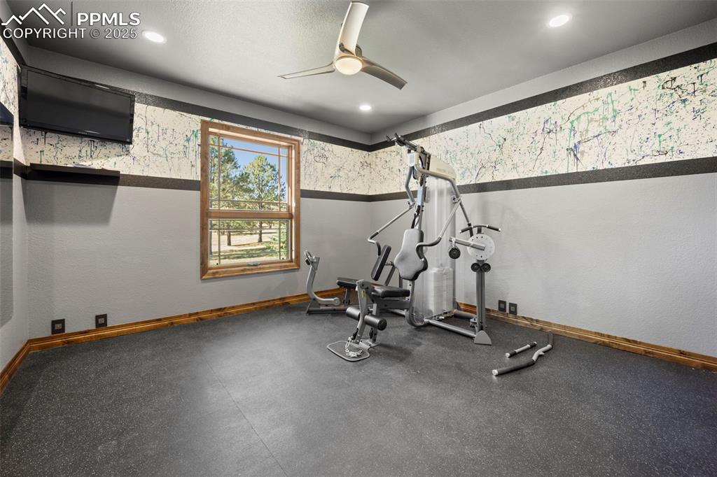 Image 37 of 50: Workout room with rubber floors, ceiling fan, and wallpapered walls