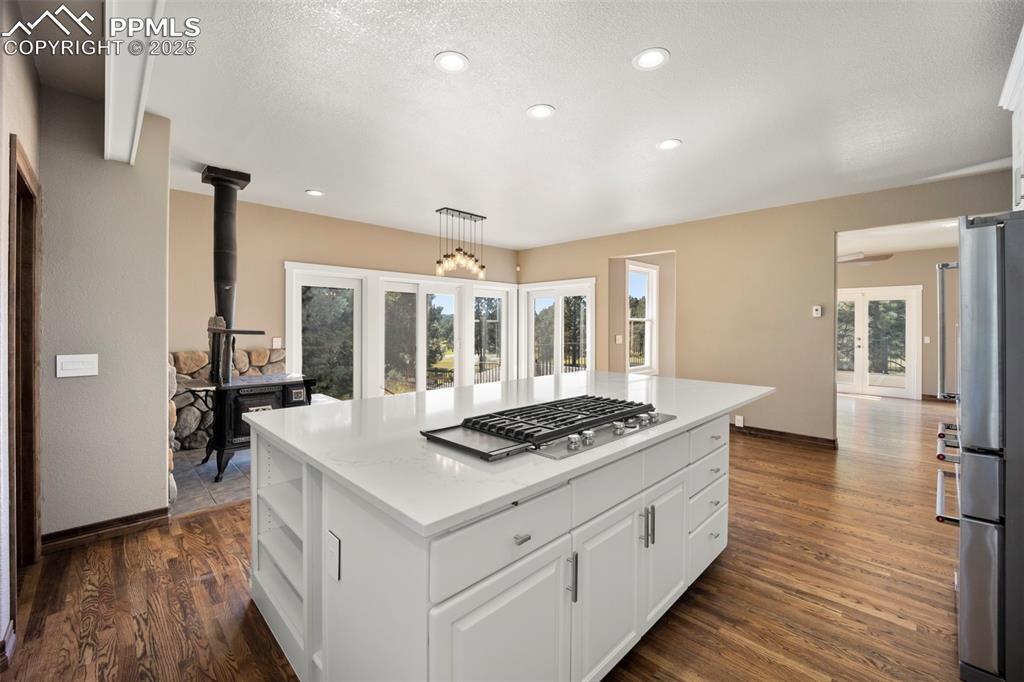 Image 8 of 50: Kitchen with a wood stove, open shelves, a kitchen island, white cabinets,