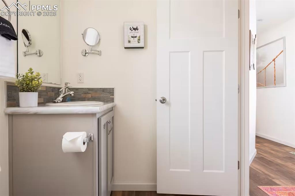 Image 13 of 26: Half bathroom with vanity, dark wood-type flooring, and decorative backspla