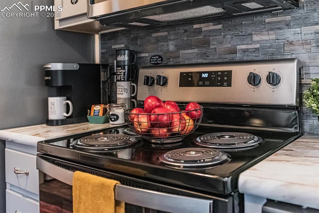 Image 9 of 26: Kitchen with stainless steel electric stove and white cabinets