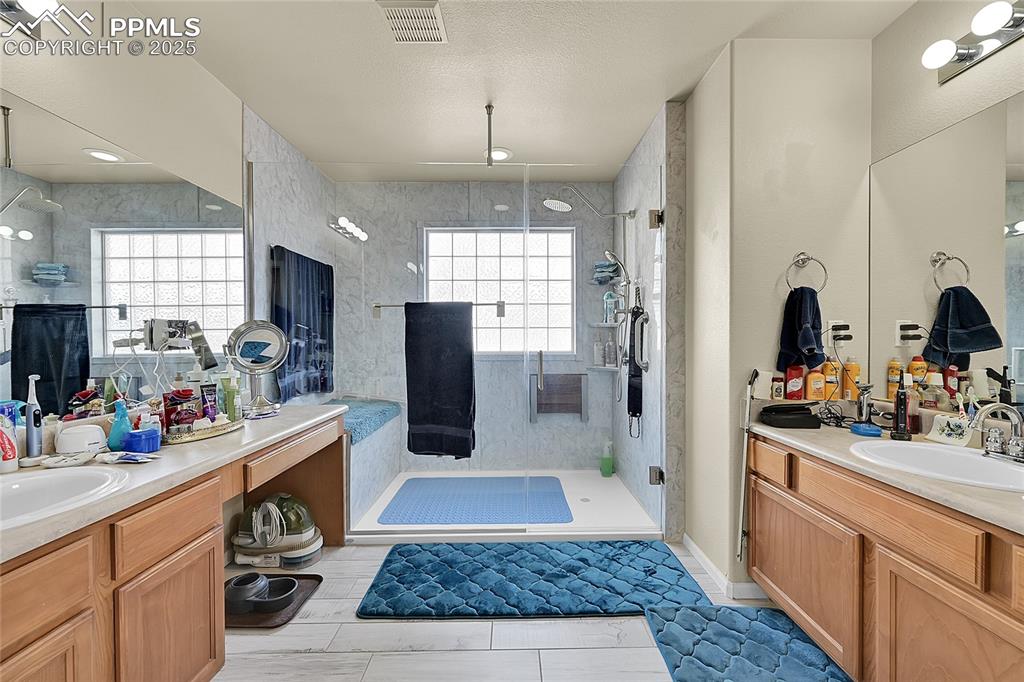 Image 23 of 44: Bathroom featuring two vanities, a stall shower, a textured ceiling, and li