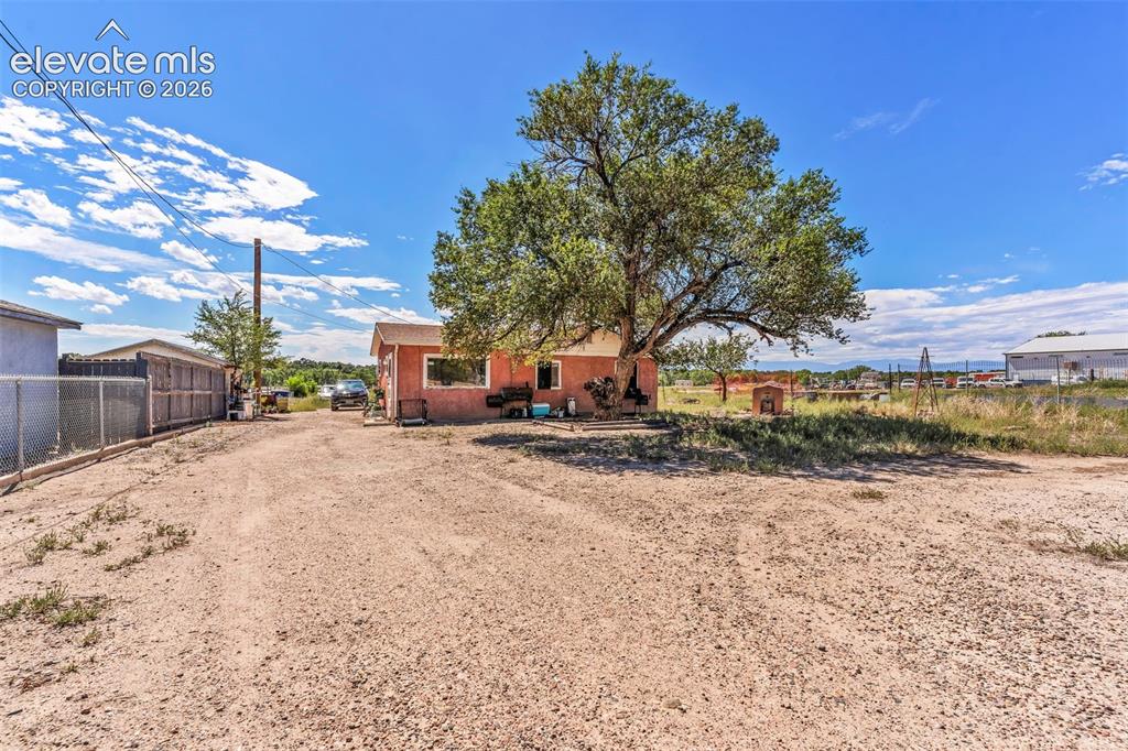 Image 24 of 29: Expansive gravel lot with mature shade tree, chain link fencing, and a red