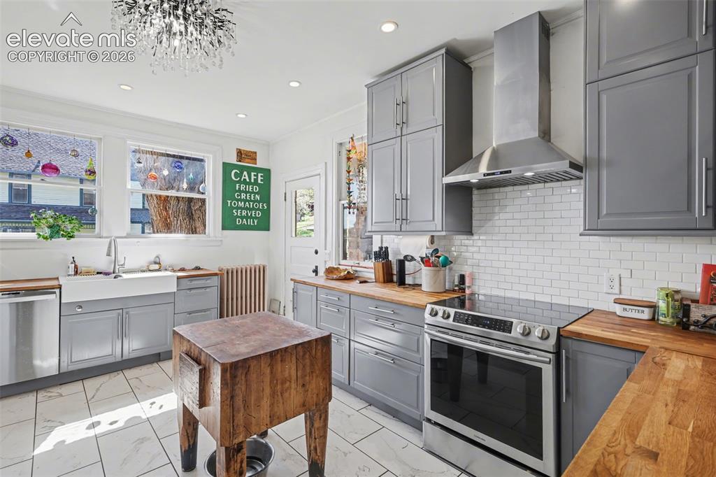 Image 16 of 43: Main house kitchen featuring gray cabinets, light tile, wood counters, and