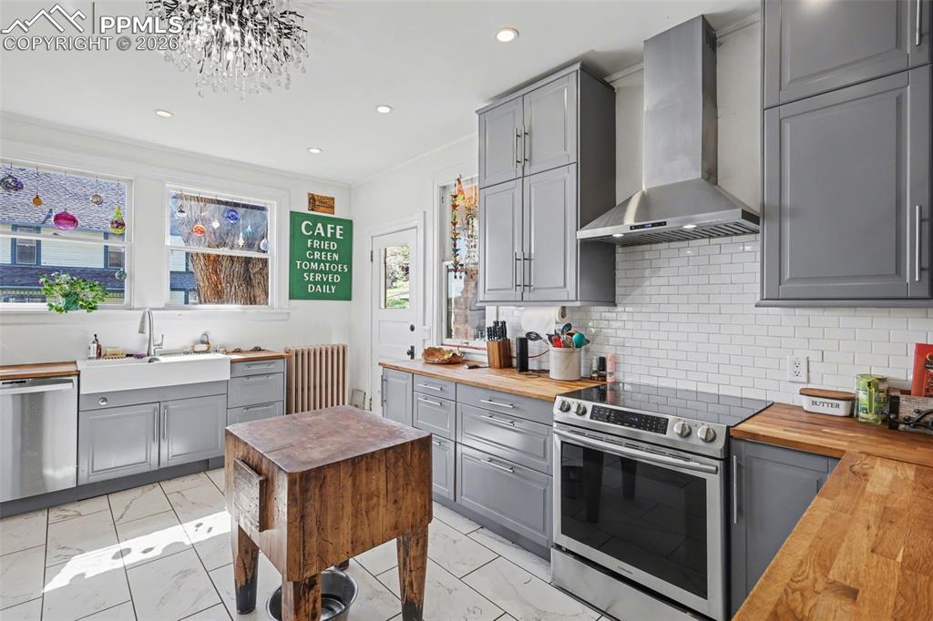Image 18 of 46: Main house kitchen featuring gray cabinets, light tile, wood counters, and 