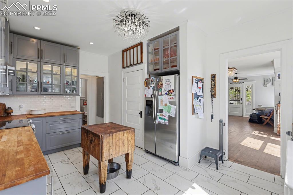 Image 19 of 46: Main house kitchen featuring gray cabinets, light tile, wood counters, and 