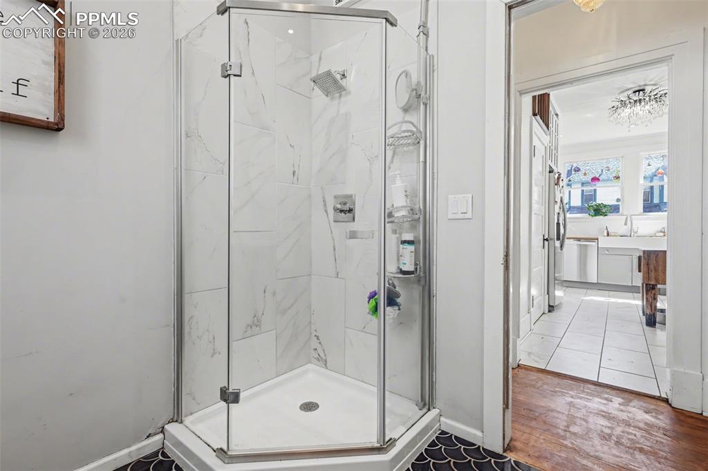 Image 21 of 46: Bathroom with a marble finish shower, hanging lights, and dark tile pattern
