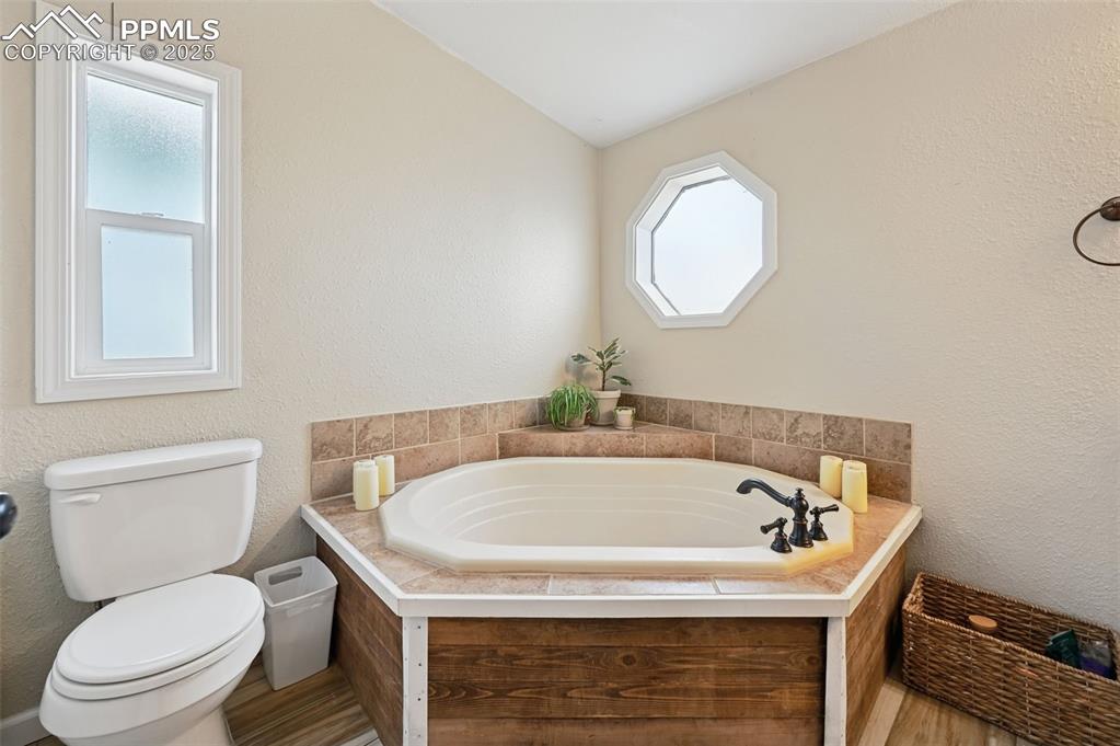 Image 12 of 31: Full bath featuring a textured wall, a garden tub, and wood finished floors