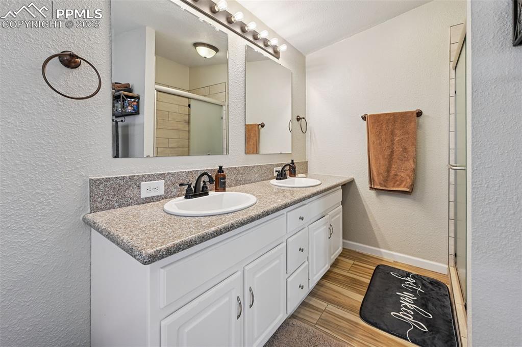 Image 13 of 31: Bathroom with a textured wall, double vanity, a stall shower, and light woo