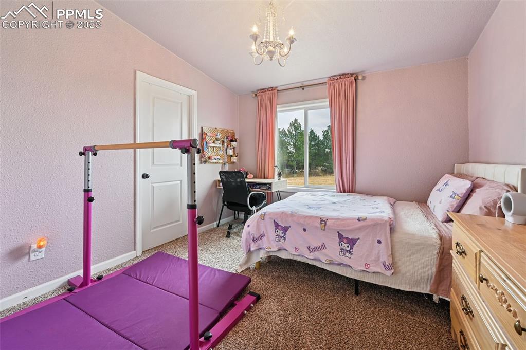 Image 16 of 31: Bedroom with a textured wall, dark colored carpet, a chandelier, and lofted