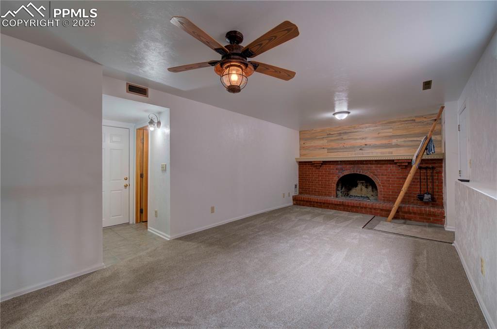 Image 26 of 50: Unfurnished living room featuring wooden walls, light carpet, a brick firep