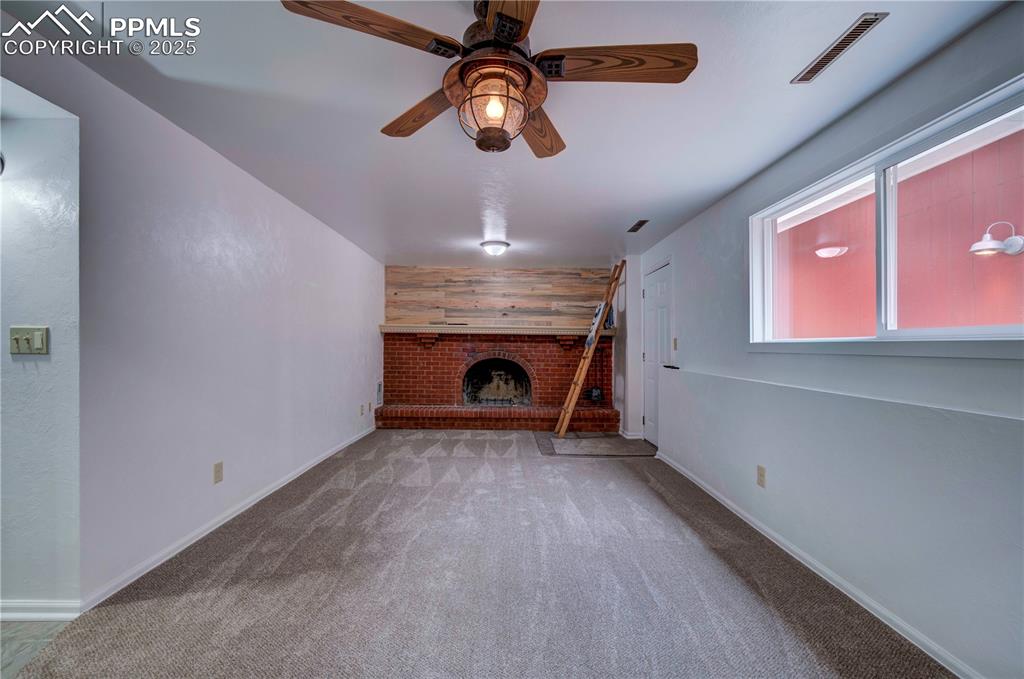Image 27 of 50: Unfurnished living room with wooden walls, ceiling fan, carpet, and a brick