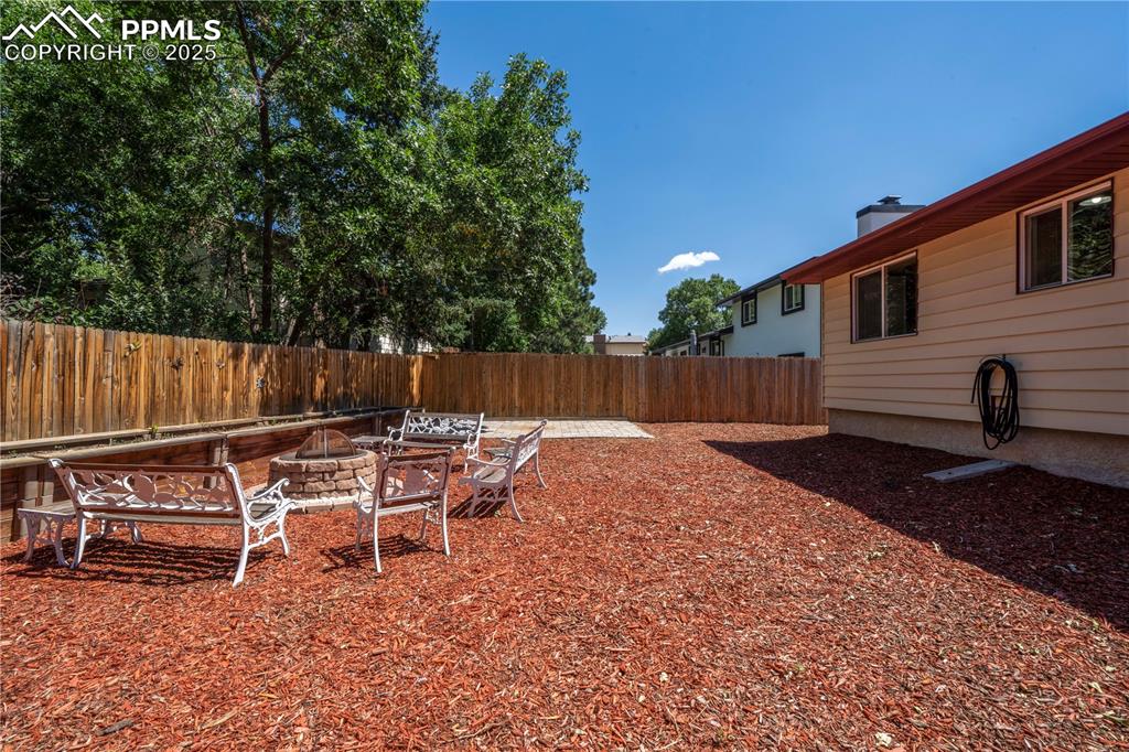Image 47 of 50: Fenced backyard with an outdoor fire pit and a patio area