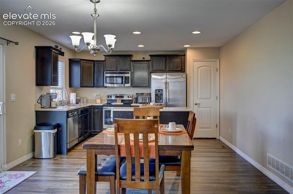 Image 16 of 45: Kitchen featuring wood-finish flooring, dark cabinetry, stainless steel app