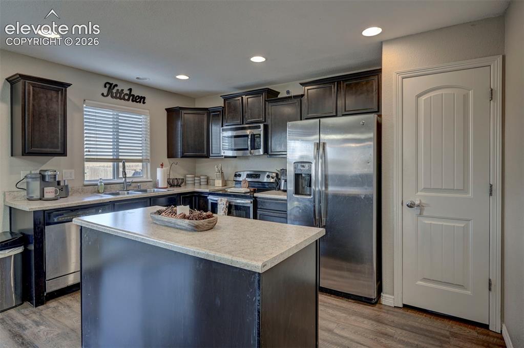 Image 18 of 45: Spacious kitchen featuring an island with a light-toned countertop, dark wo