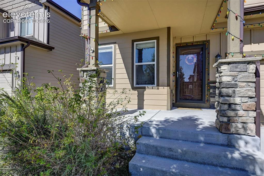 Image 8 of 45: Entry porch with stone-clad columns, concrete steps, and a storm door