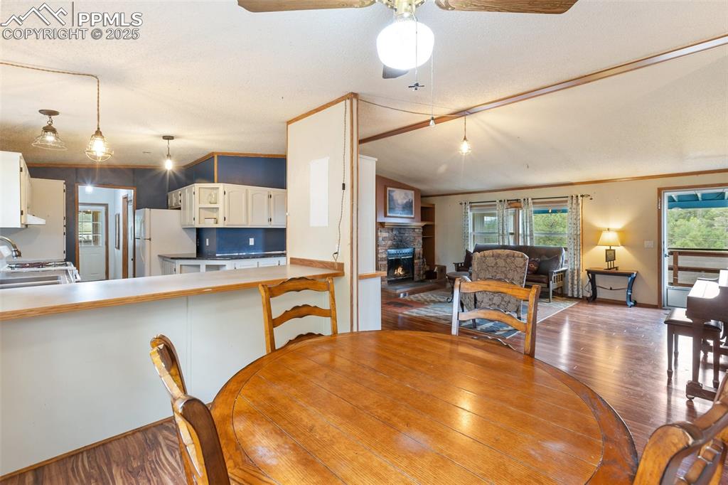 Image 14 of 37: Dining area with wood finished floors, ornamental molding, a fireplace, vau