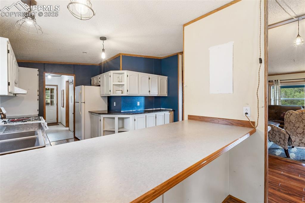 Image 19 of 37: Kitchen with ornamental molding, white cabinets, hanging light fixtures, an