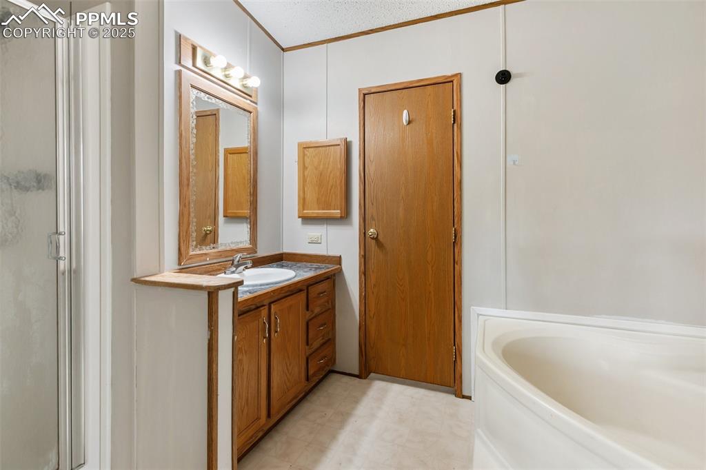 Image 28 of 37: Full bath with a stall shower, vanity, a garden tub, a textured ceiling, an
