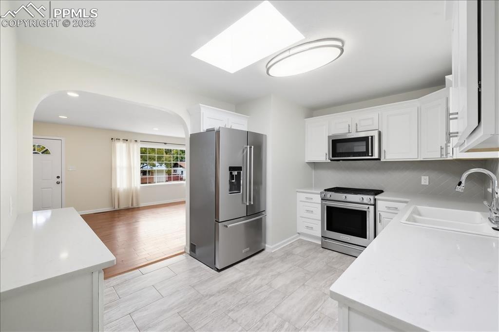 Image 10 of 22: Kitchen with appliances with stainless steel finishes, a skylight, white ca
