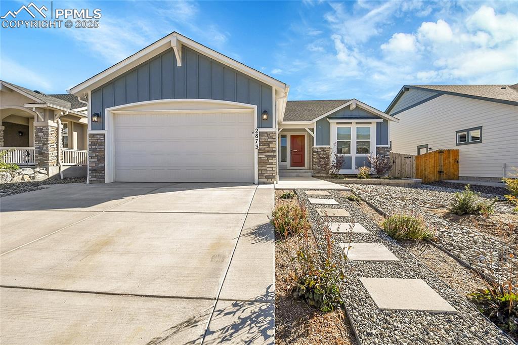 Caption: View of front facade with board and batten siding, stone siding, a garage, and concrete driveway