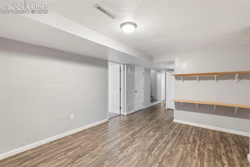 Image 17 of 25: Finished basement with dark wood/laminate-style flooring and a textured cei