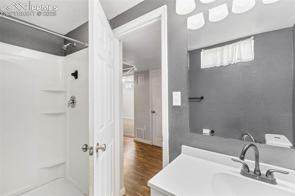 Image 20 of 25: 3/4 bath featuring a stall shower, vanity, a textured wall, and dark wood/l