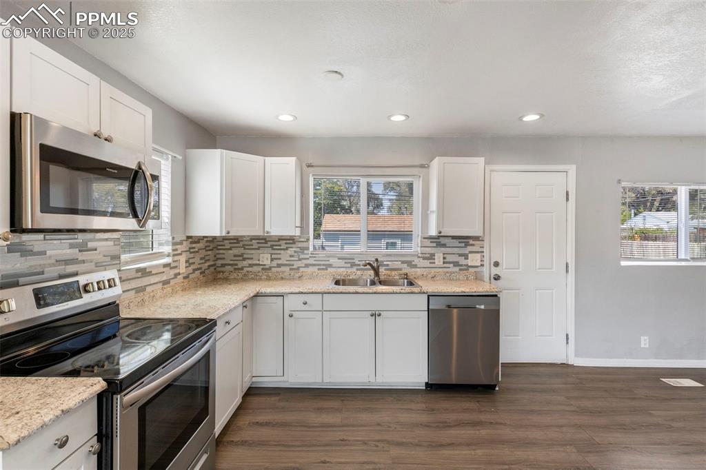Image 6 of 25: Kitchen with appliances with stainless steel finishes, white cabinetry, bac