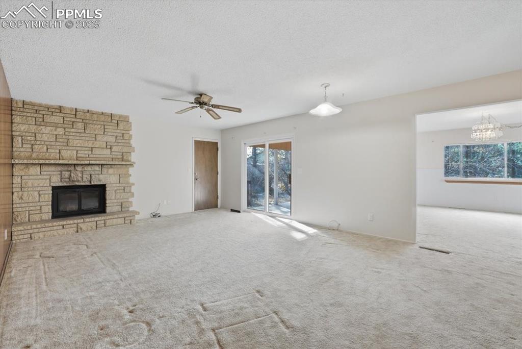 Image 28 of 50: Unfurnished living room featuring a stone fireplace, a textured ceiling, ca