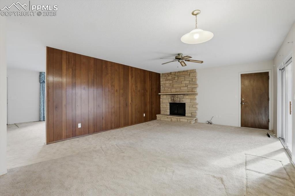 Image 29 of 50: Unfurnished living room featuring wooden walls, ceiling fan, light carpet, 