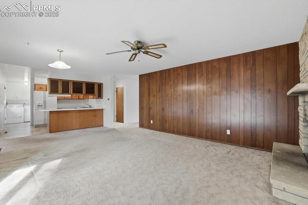 Image 30 of 50: Unfurnished living room featuring wood walls, ceiling fan, and light colore