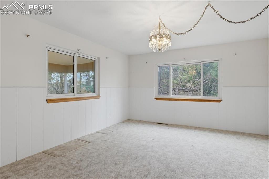 Image 32 of 50: Carpeted spare room with wainscoting and a chandelier
