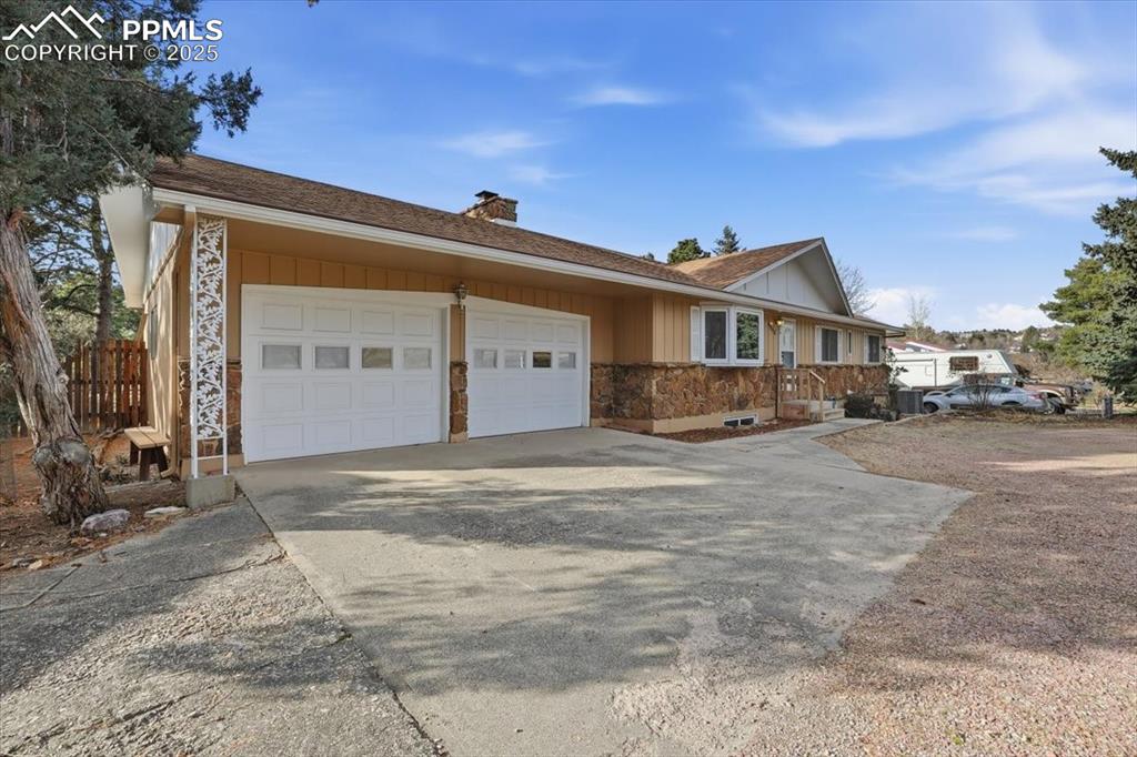 Image 6 of 50: Ranch-style house featuring a chimney, driveway, stone siding, and a garage
